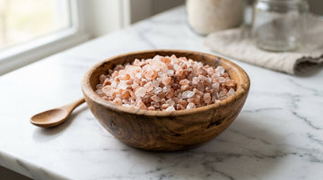 Pink Himalayan salt crystals in a wooden bowl on white marble
